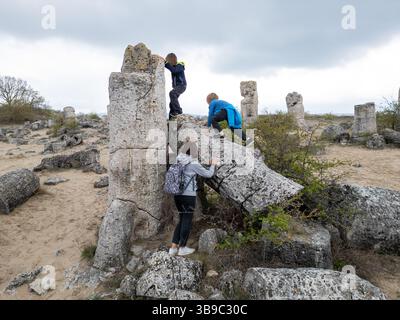 Madre e due bambini esplorano il terreno roccioso in un paesaggio arido e semi-desertico. I bambini giocano su formazioni di pietra mentre la madre guarda, enjo Foto Stock