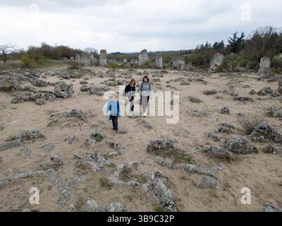 Madre e due bambini esplorano il terreno roccioso in un paesaggio arido e semi-desertico. I bambini giocano su formazioni di pietra mentre la madre guarda, enjo Foto Stock