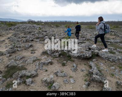 Madre e due bambini esplorano il terreno roccioso in un paesaggio arido e semi-desertico. I bambini giocano su formazioni di pietra mentre la madre guarda, enjo Foto Stock