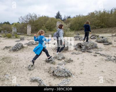 Madre e due bambini esplorano il terreno roccioso in un paesaggio arido e semi-desertico. I bambini giocano su formazioni di pietra mentre la madre guarda, enjo Foto Stock