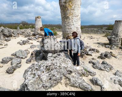 Madre e due bambini esplorano il terreno roccioso in un paesaggio arido e semi-desertico. I bambini giocano su formazioni di pietra mentre la madre guarda, enjo Foto Stock