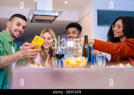 Amici multietnici felici gustando spuntini e bevande in una cucina moderna e luminosa Foto Stock