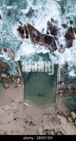 Una vista aerea dall'alto verso il basso delle rocce aspre di Camps Bay, città del Capo, che mostra le strutture uniche della costa rocciosa Foto Stock