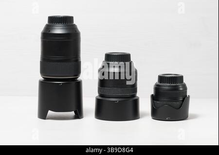 Tre obiettivi per fotocamera neri di diverse dimensioni in posizione verticale su una superficie bianca con sfondo bianco, senza persone, primi piani. Foto Stock