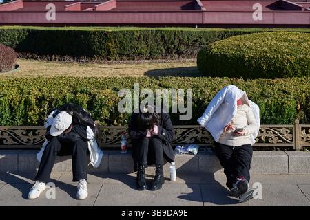 Turisti esausti che riposano su una panchina all'esterno della porta Tiananmen a Pechino in una giornata di sole Primavera Foto Stock