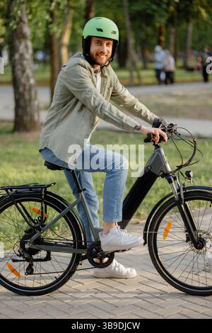 Un uomo sorridente corre in bicicletta elettrica in un parco durante una giornata di sole Foto Stock