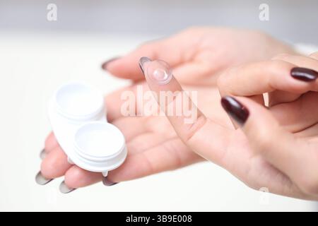 Primo piano di una donna che tiene una lente a contatto. FingerTIP con manicure. Apri la custodia per lenti a contatto in mano. Concetto di correzione della vista, igiene e cura degli occhi. Foto Stock