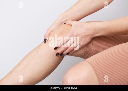 Donna che tocca il ginocchio dolorante. Massaggio antidolorifico. Terapia per le gambe di primo piano. Infortunio sportivo fastidio. Concetto di assistenza sanitaria. Trattamento del dolore muscolare. Foto Stock