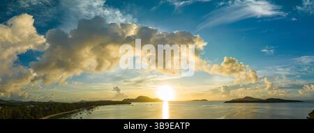 Una vibrante scena tropicale dell'alba caratterizzata da cieli colorati, acque tranquille e barche che galleggiano dolcemente sul mare. Le tonalità vivaci e l'atmosfera tranquilla Foto Stock