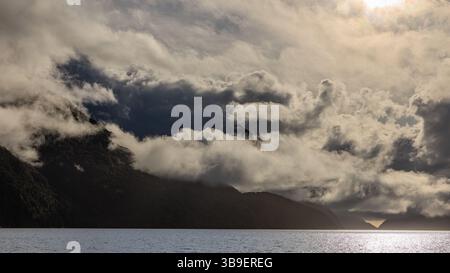 suggestivo paesaggio di formazioni nuvolose che pendono in basso sulle ripide pareti scure di suoni dubbiosi nel fiordland nuova zelanda Foto Stock