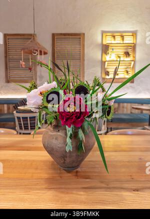 Vaso rustico in terracotta con peonie e girasoli su tavolo in legno nell'accogliente Cafe interno Foto Stock