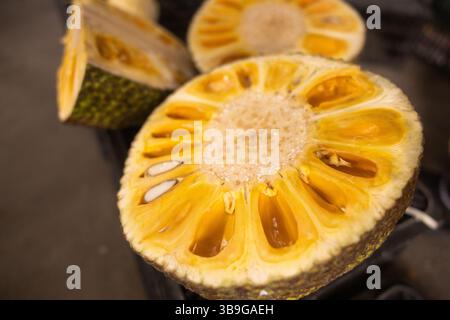 Primo piano di jackfruit maturi tagliati a metà in un eco-mercato vietnamita, caratterizzato dalla polpa gialla vibrante e dai semi. La trama e il colore evidenziano la tropica Foto Stock