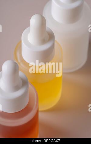 Questa foto stock presenta un trio di flaconi contagocce riempiti con liquidi arancioni, gialli e traslucidi, su un morbido sfondo beige. Foto Stock