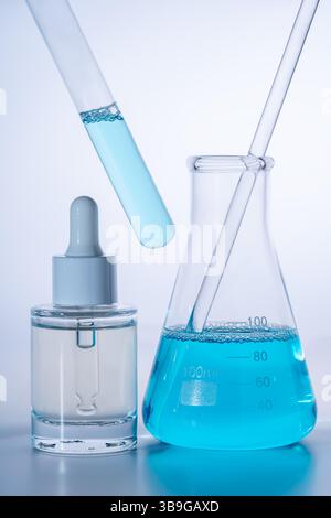 Configurazione del laboratorio con flacone contagocce, provetta per analisi e becher riempiti con liquido blu vivace, che presenta un'atmosfera scientifica e sperimentale Foto Stock