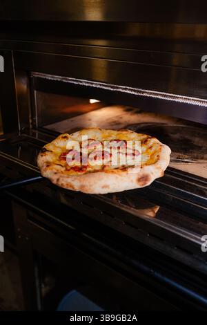 Una deliziosa pizza condita con fette di peperoni e formaggio fuso, appena sfornata in un forno caldo. Immagine perfetta per evocare l'aroma e il gusto della cucina italiana Foto Stock