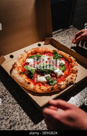 Una deliziosa pizza margherita condita con basilico fresco e mozzarella, presentata in una scatola di cartone, pronta per essere servita. Perfetto per un pasto accogliente e saporito Foto Stock