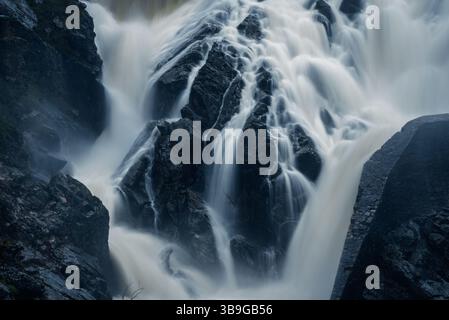Un'affascinante fotografia a lunga esposizione che cattura l'acqua liscia e fluente che si getta sulle rocce aspre di presa del Villar, Madrid, creando un tranqui Foto Stock