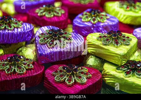 Caramelle al cioccolato multicolore a forma di cuore in un involucro lucido con spilla regalo, vista dall'alto. Foto Stock