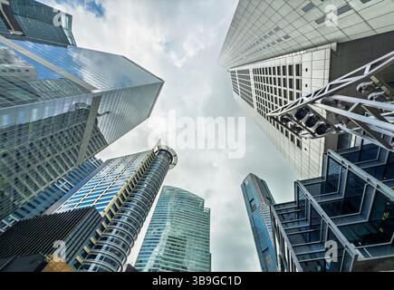 Una vista verso l'alto che cattura l'architettura dinamica di grattacieli torreggianti sotto un cielo nuvoloso in un quartiere finanziario di Singapore. Foto Stock