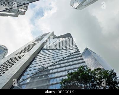 Da sotto una dinamica vista verso l'alto dei grattacieli moderni torreggianti di Singapore, adagiati su un cielo nuvoloso, che mostrano architettura e design urbani. Foto Stock
