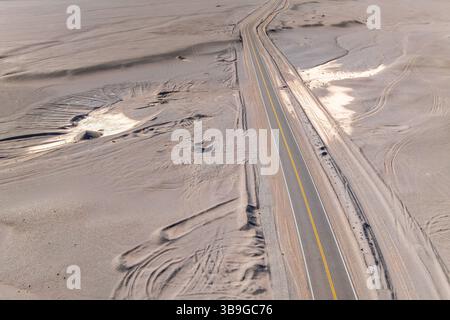 Vista aerea di una lunga e solitaria strada asfaltata che attraversa un vasto paesaggio desertico della Puna argentina. La scena cattura la vastità e. Foto Stock