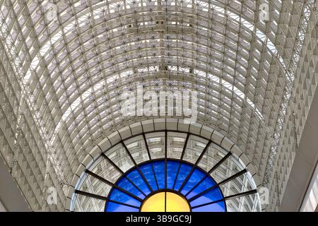 Immagine architettonica dell'interno di un edificio. Una struttura ricurva a motivi geometrici domina, con una finestra circolare in vetro colorato sotto al Bentall Cent Foto Stock
