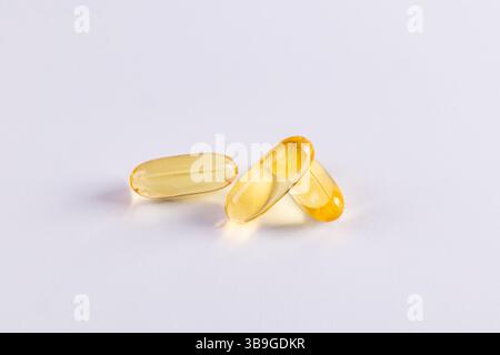 Un primo piano di capsule di omega 3 traslucide e di gelatina di vitamina e disposte su una superficie bianca pulita. Le capsule sono dorate e lucenti, incarnano lui Foto Stock