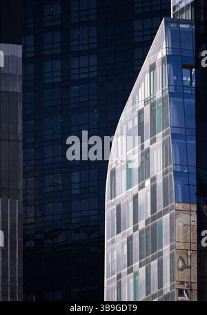 Moderno edificio in vetro dal design curvo contrasta nettamente con uno sfondo di torri metalliche scure e riflettenti a New York. L'immagine acquisisce Foto Stock