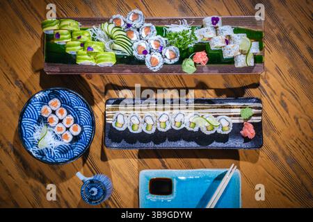 Vista dall'alto di una varietà di coloratissimi sushi roll serviti su piatti decorativi, pronti da gustare con salsa di soia e bacchette, creando un vivace culin Foto Stock