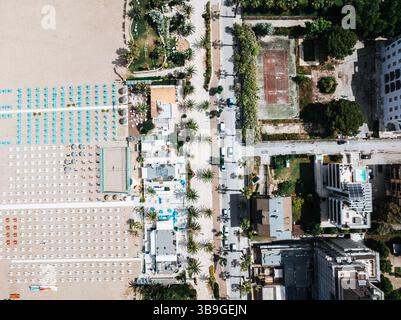 Foto aerea dall'alto verso il basso che mostra gli ombrelloni organizzati sulla costa di San Benedetto in Italia, adiacente a strade, edifici, palme e un Foto Stock
