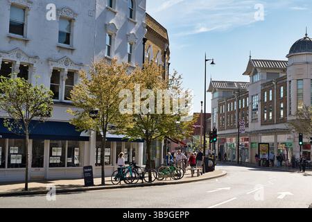 Scena di strada con edifici, alberi, persone e biciclette parcheggiate lungo il marciapiede in una giornata di sole a Wimbledon, Londra, Regno Unito. Foto Stock