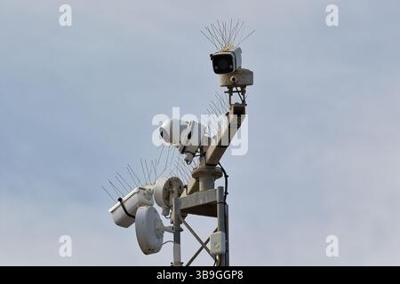 Tre telecamere di sorveglianza montate su un palo metallico, che puntano in direzioni diverse, poste contro un cielo azzurro. Foto Stock