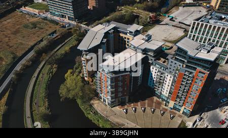 Veduta aerea dei moderni condomini lungo un fiume, con infrastrutture urbane e spazi verdi. Foto di sole diurne a Leeds, Regno Unito. Foto Stock