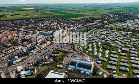 Veduta aerea di una città che confina con i campi e di un parco per roulotte. Dispone di case, automobili, strade, spazi verdi e un edificio a pannelli solari nel villaggio Seahouses Foto Stock