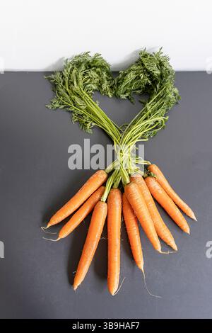Il verde sul mucchio di carote disposte come forma di cuore sul tema del mangiare sano Foto Stock