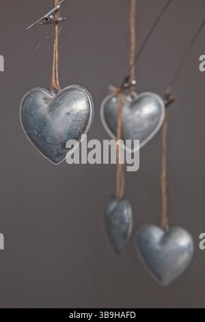 Cuori in metallo color argento appesi su corde in primo piano su sfondo grigio come messaggio simbolico e decorazione per il matrimonio Foto Stock