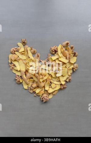 I frammenti di patate e le pelature si trovano a forma di cuore su sfondo grigio sul tema dei rifiuti organici e della separazione organica Foto Stock