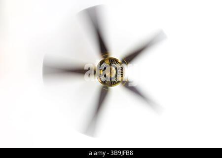 Un ventilatore a soffitto che gira con movimento visibile sfocato su un soffitto bianco Foto Stock
