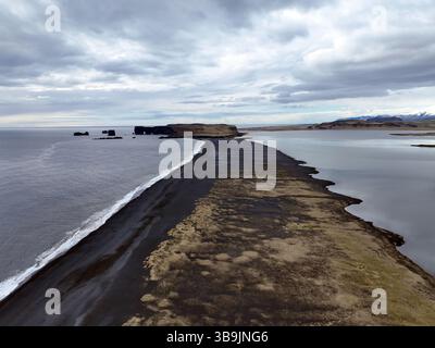 Vista aerea che cattura il forte contrasto della spiaggia di sabbia nera di Reynisfjara che incontra il turbolento Oceano Atlantico settentrionale Foto Stock