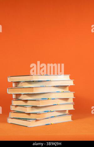 I libri sono impilati uno sopra l'altro su uno sfondo arancione Foto Stock