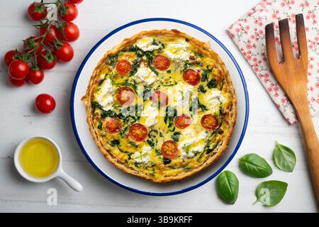 Quiche francese con spinaci, formaggio, pomodori e prosciutto a dadini. Tavolo con vista dall'alto e decorazioni natalizie. Foto Stock
