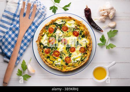 Quiche francese con spinaci, formaggio, pomodori e prosciutto a dadini. Tavolo con vista dall'alto e decorazioni natalizie. Foto Stock