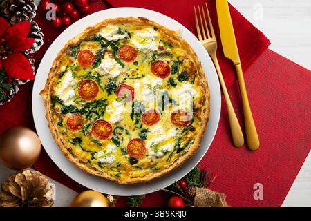 Quiche francese con spinaci, formaggio, pomodori e prosciutto a dadini. Tavolo con vista dall'alto e decorazioni natalizie. Foto Stock