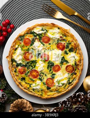 Quiche francese con spinaci, formaggio, pomodori e prosciutto a dadini. Tavolo con vista dall'alto e decorazioni natalizie. Foto Stock