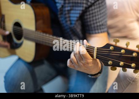 Primo piano dettagliato della mano di un uomo che preme corde sul collo di una chitarra. Intima ripresa di pratica e tecnica musicale, scattata al chiuso in un ambiente rilassato Foto Stock