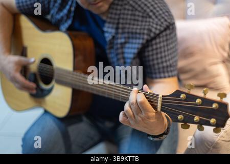 Primo piano dettagliato della mano di un uomo che preme corde sul collo di una chitarra. Intima ripresa di pratica e tecnica musicale, scattata al chiuso in un ambiente rilassato Foto Stock