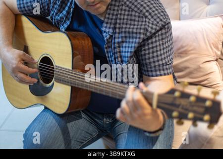 Primo piano dettagliato della mano di un uomo che preme corde sul collo di una chitarra. Intima ripresa di pratica e tecnica musicale, scattata al chiuso in un ambiente rilassato Foto Stock