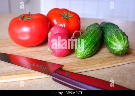 Cetrioli freschi, ravanelli e pomodori su un tagliere con un primo piano di coltelli Foto Stock