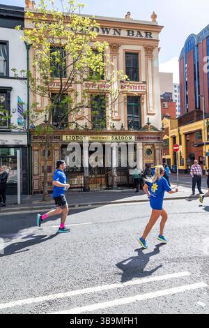I corridori della maratona di Belfast corrono davanti al famoso Crown Bar di Belfast. Foto Stock