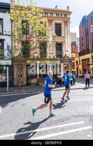 I corridori della maratona di Belfast corrono davanti al famoso Crown Bar di Belfast. Foto Stock